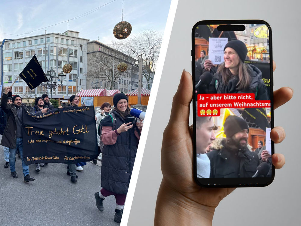 Des personnes tenant une bannière noire manifestent dans une rue aux décorations de fête et aux stands de marché. Une main tient un téléphone montrant la scène.