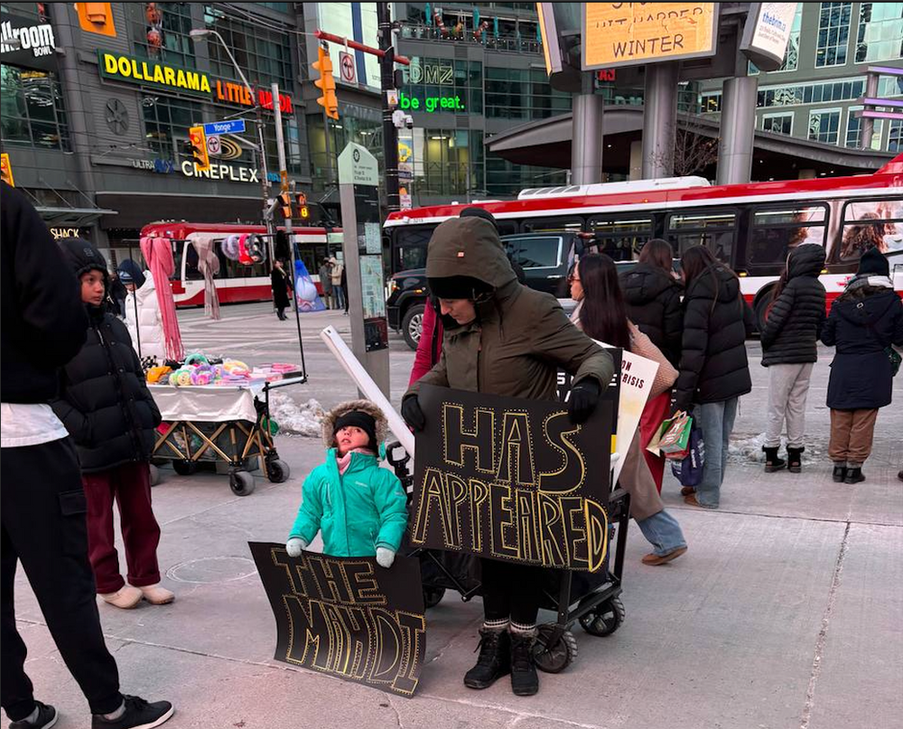 Cinq membres tiennent des bannières noires proclamant « Le Mahdi est apparu » et « Seul Dieu peut choisir un dirigeant » dans le centre-ville animé de Toronto, le 14 décembre 2025.