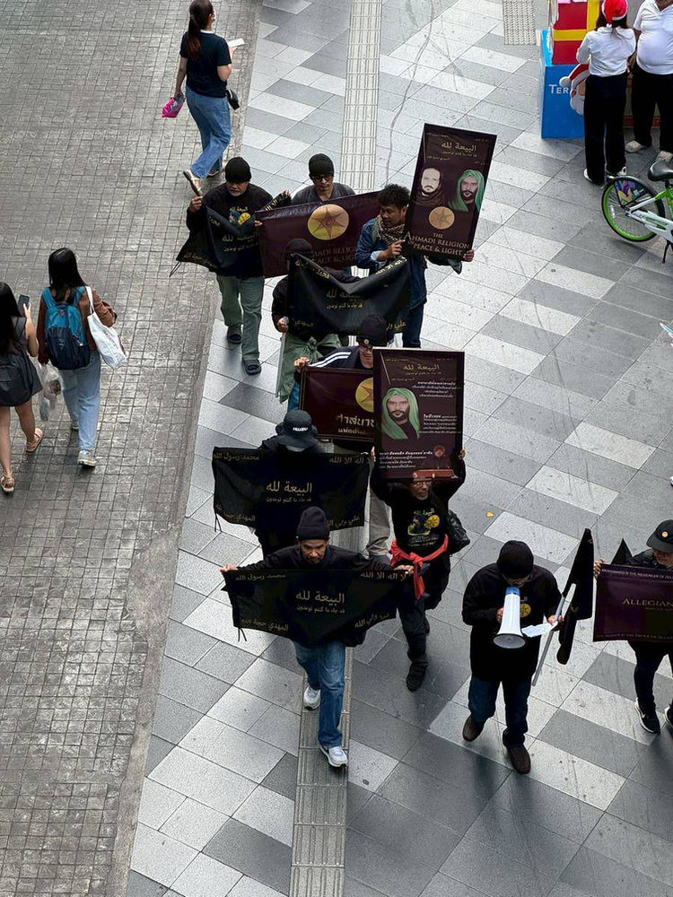 Quinze croyants thaïlandais dévoués de la Religion Ahmadie de la Paix et de la Lumière défilent devant le Siam Paragon, à Bangkok, levant fièrement la bannière « L’allégeance est à Allah » durant la campagne mondiale du Ramadan de décembre.