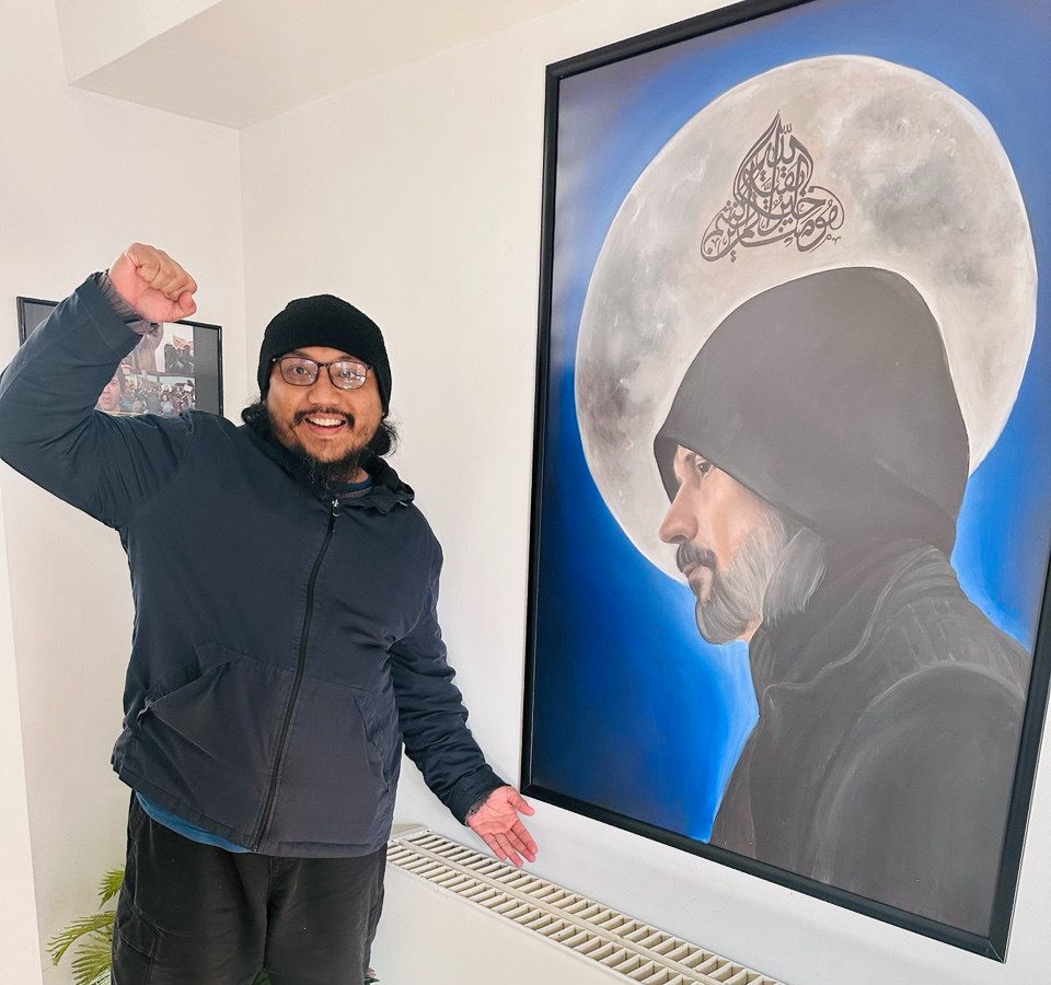 Ahmad Bukhari à côté d’un portrait du Qaim/Riseur, Abdullah Hashem Aba Al-Sadiq