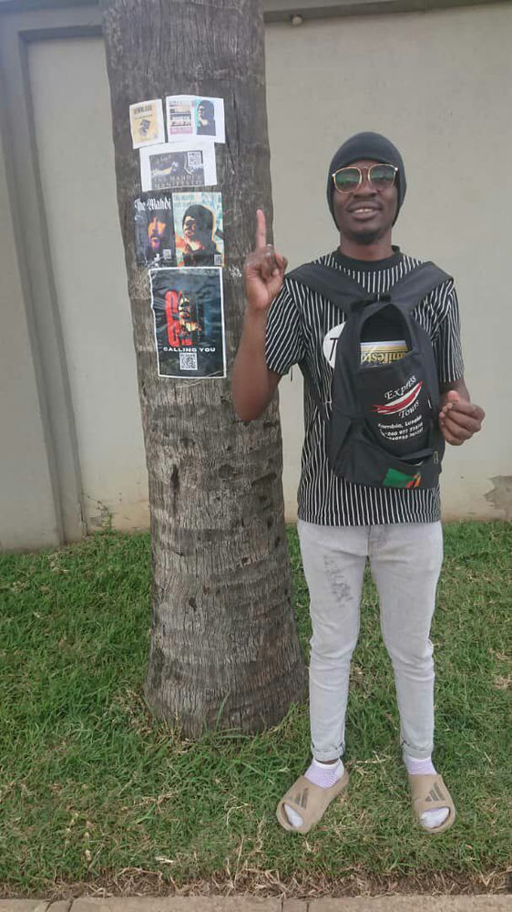 Zambian follower of Aba Al-Sadiq next to a flyer