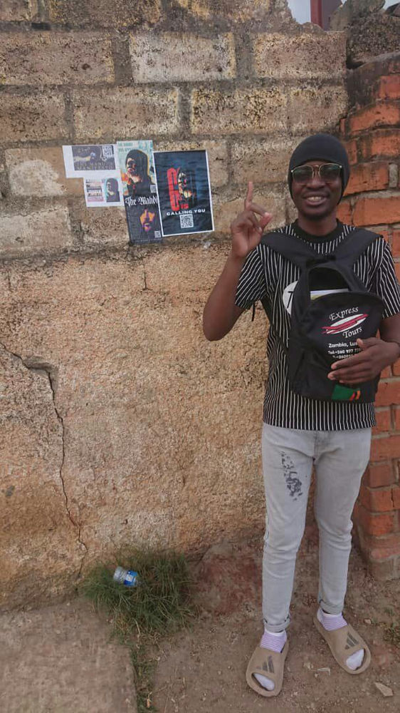 Zambian follower of Aba Al-Sadiq next to a flyer