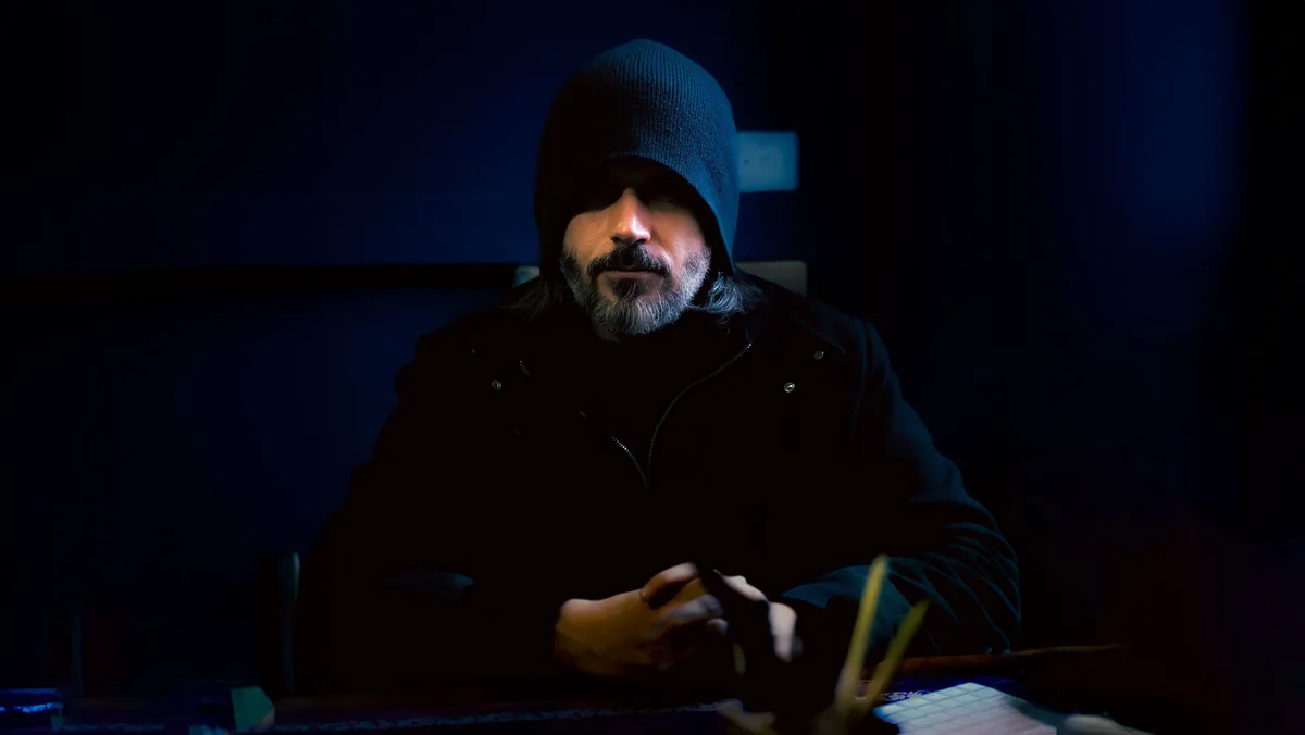 Abdullah Hashem Aba Al-Sadiq, assis à une table, vêtu d’une veste à capuche sombre, dans une pièce faiblement éclairée.