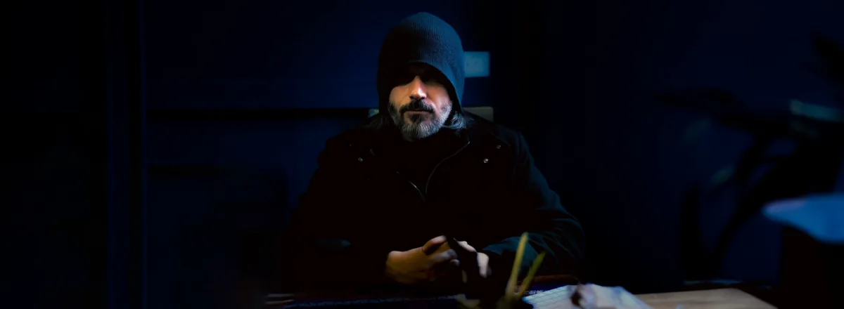 Abdullah Hashem Aba Al-Sadiq, assis à une table, vêtu d’une veste à capuche sombre, dans une pièce faiblement éclairée.